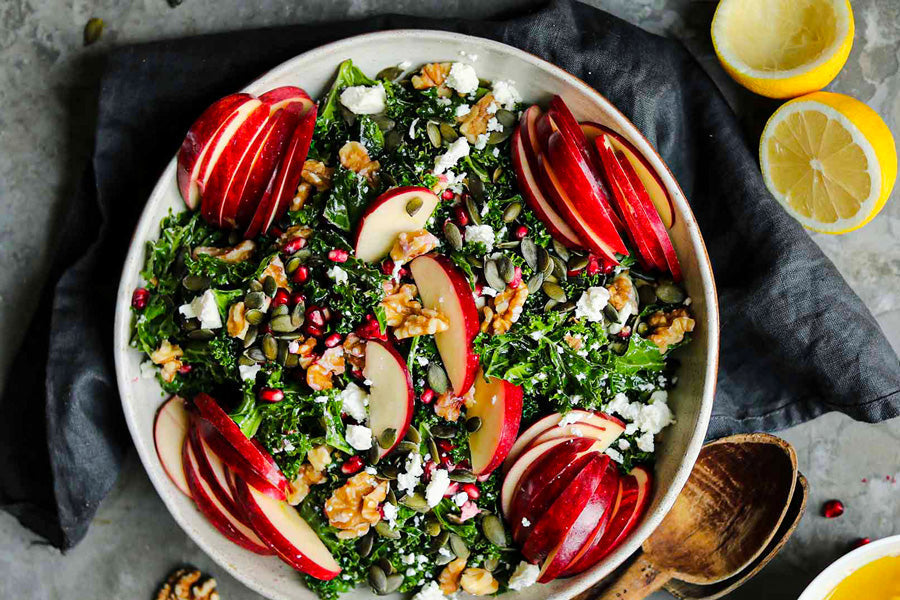 fresh kale apple and walnut salad in a big bowl on a cement table with fresh lemons.